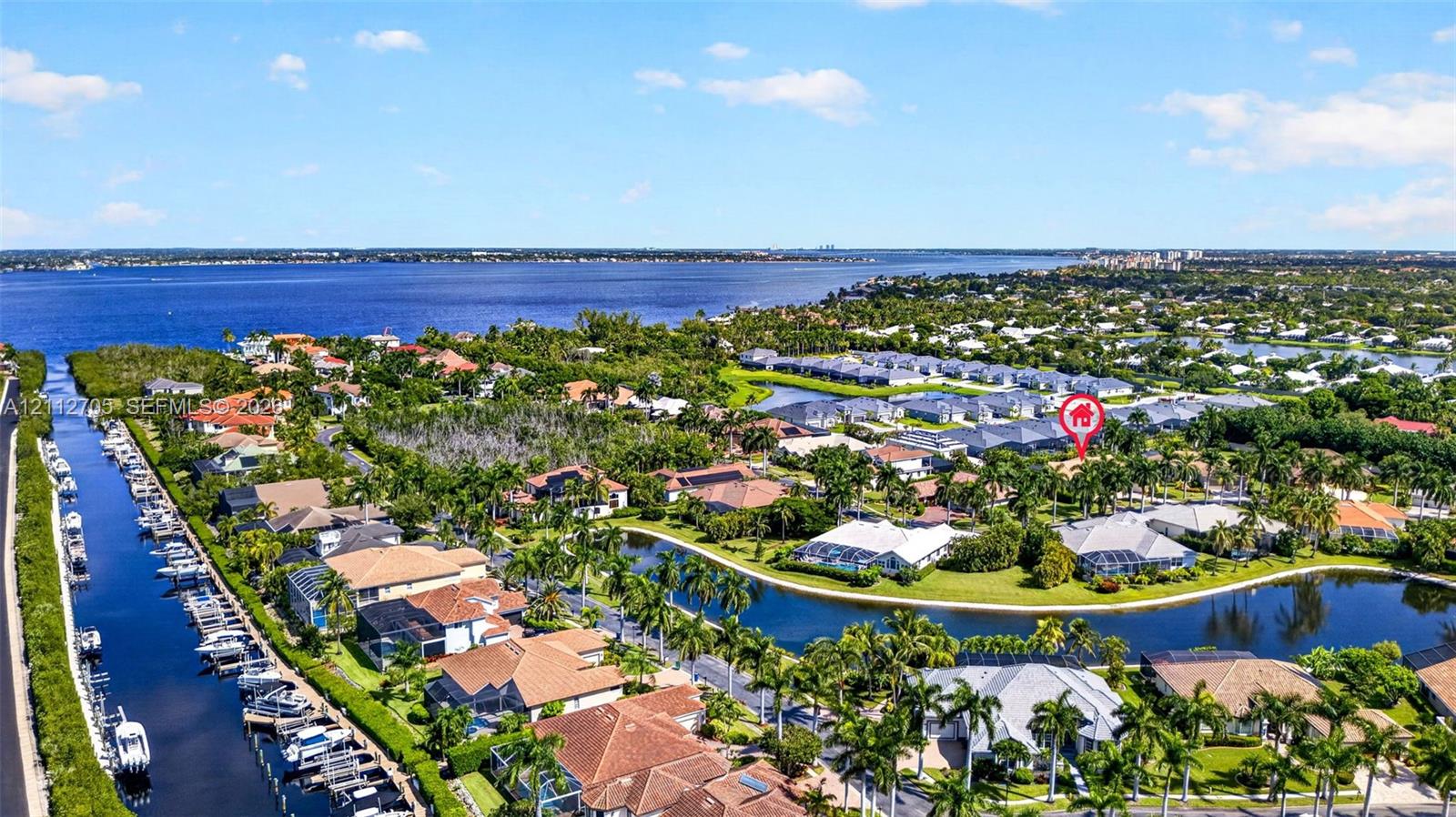 Aerial perspective of a coastal residential community featuring waterfront property, a winding canal, mature landscaping, and proximity to the bay