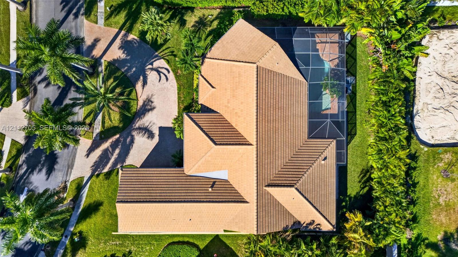 Aerial view featuring a multi-hipped tile roof, a screen-enclosed pool, a paved circular driveway, and mature landscaping
