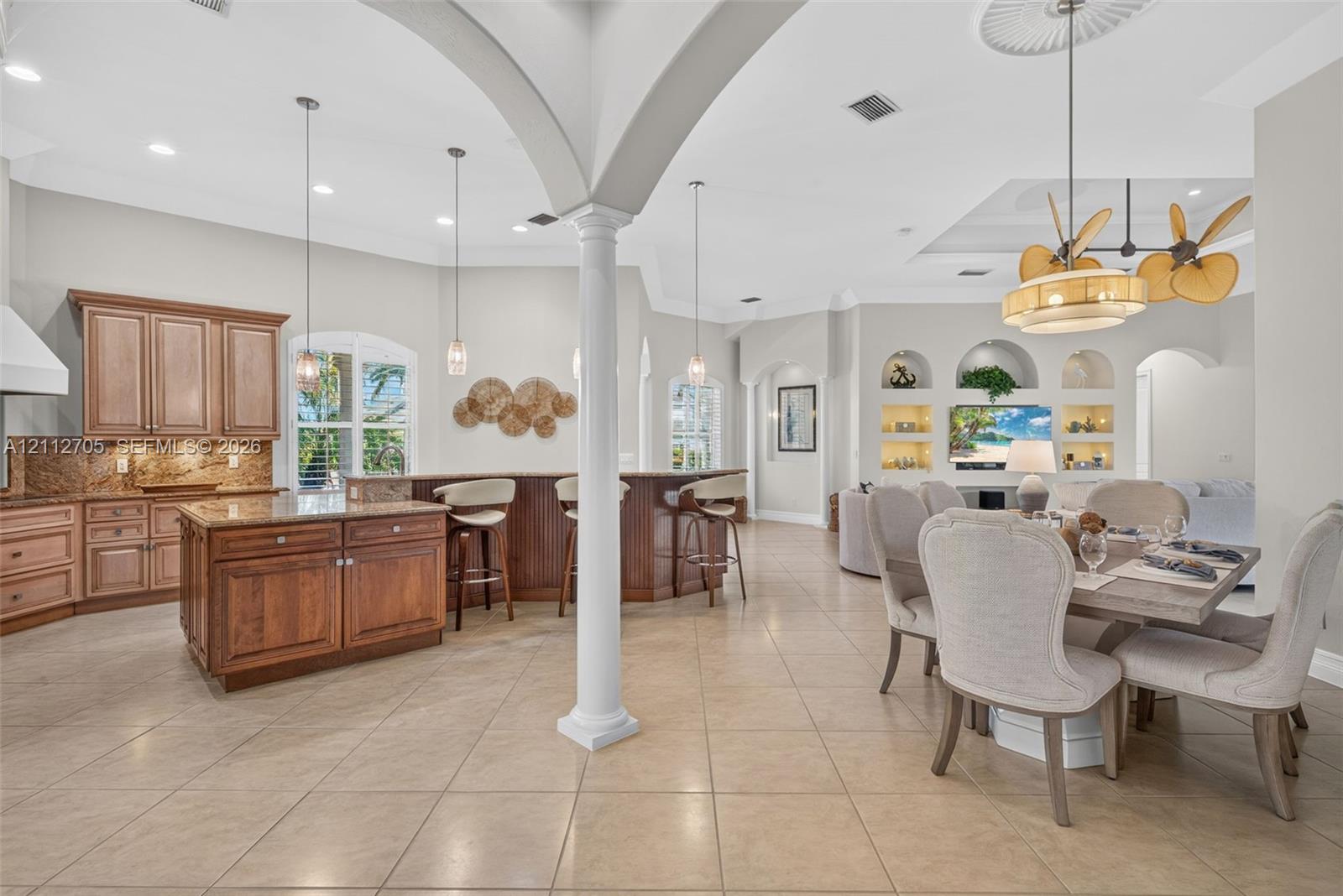 Open-concept interior featuring wood cabinetry, stone countertops, architectural columns, tile flooring, and built-in wall niches
