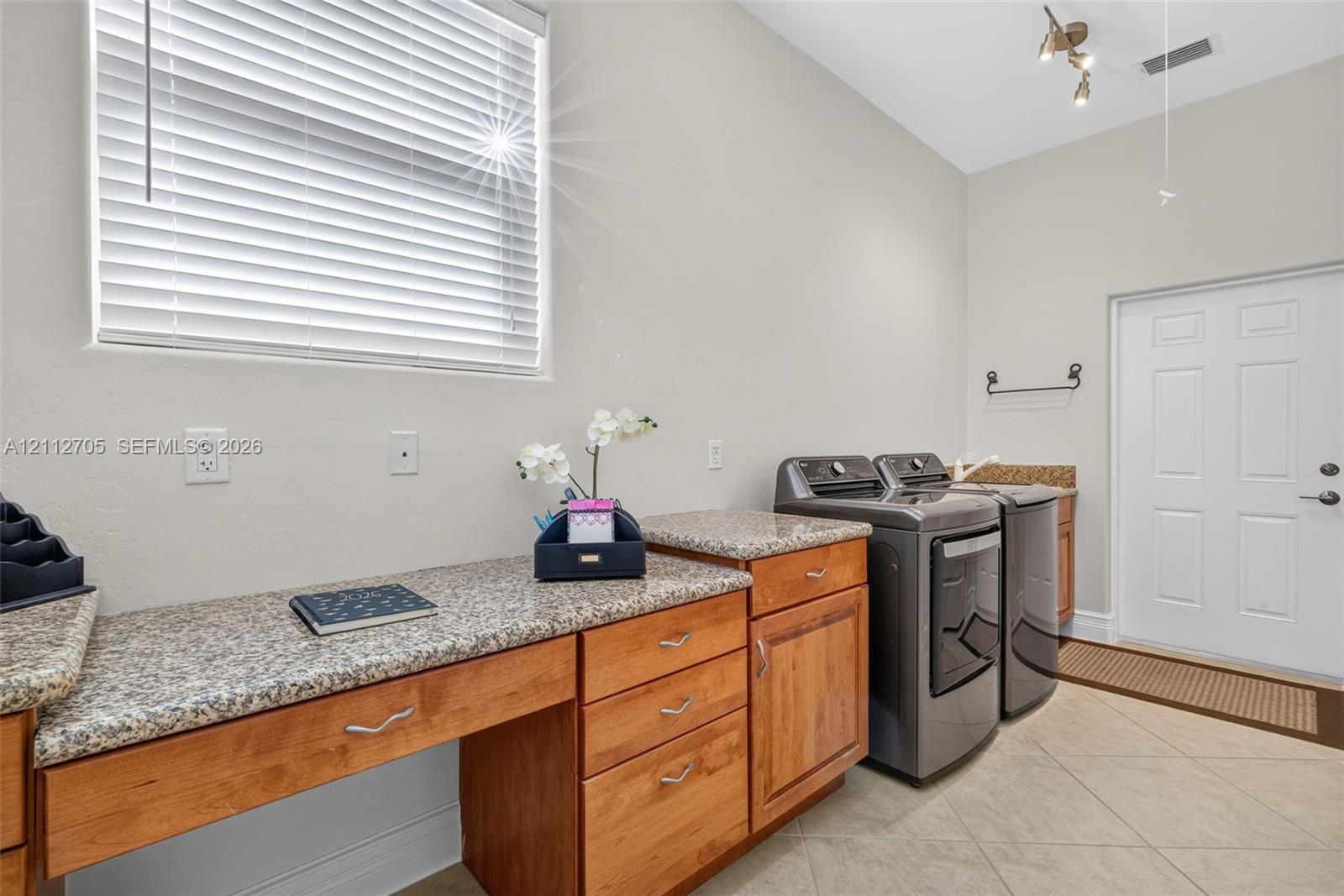 Laundry area featuring extensive wood cabinetry, stone-finish countertops, tile flooring, and a large window with horizontal blinds