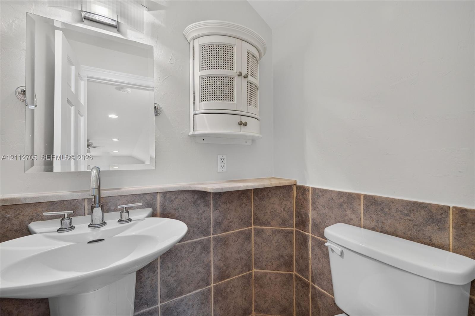 Pedestal sink with polished chrome widespread faucet, wall-mounted mirrored cabinet, built-in corner storage unit, and tile wainscoting