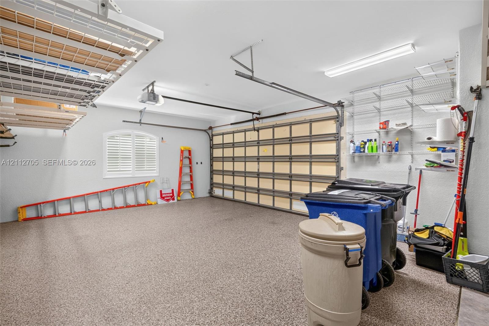 Garage featuring an epoxy floor finish, overhead mounted storage racks, wall-mounted wire shelving, and an arched window with shuttered treatment