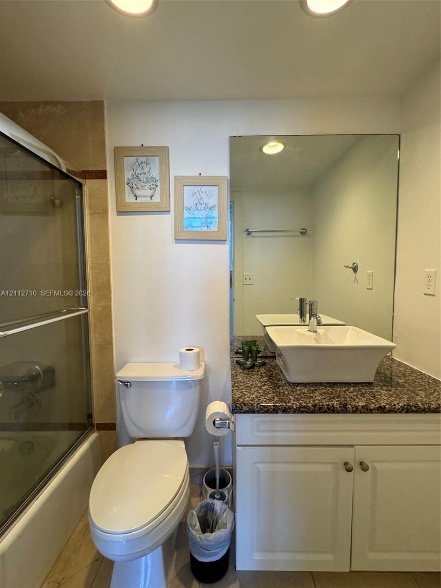 Bathroom featuring a vanity with a stone-surface countertop, a white rectangular vessel sink, a full-width wall mirror, and a tub-shower combination with a sliding glass enclosure