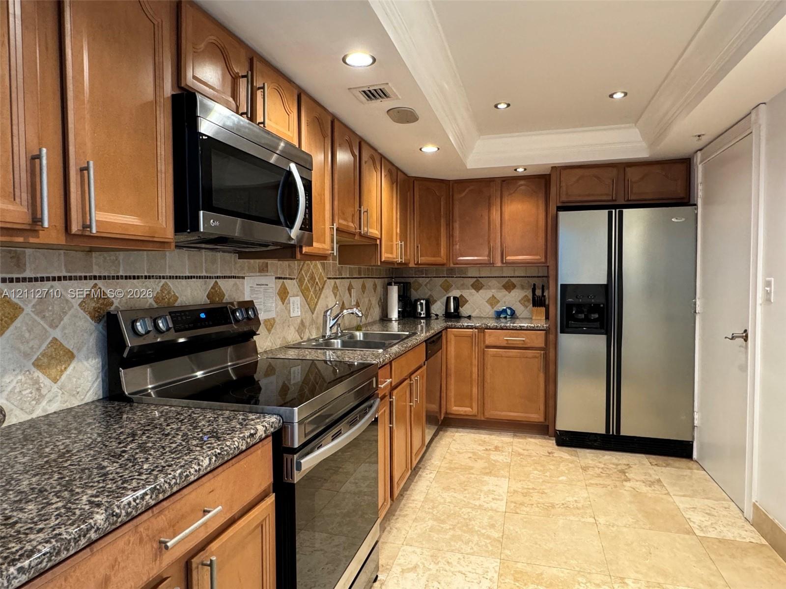 Kitchen featuring wood cabinetry, stone countertops, stone tile backsplash, stainless steel appliances, and tile flooring
