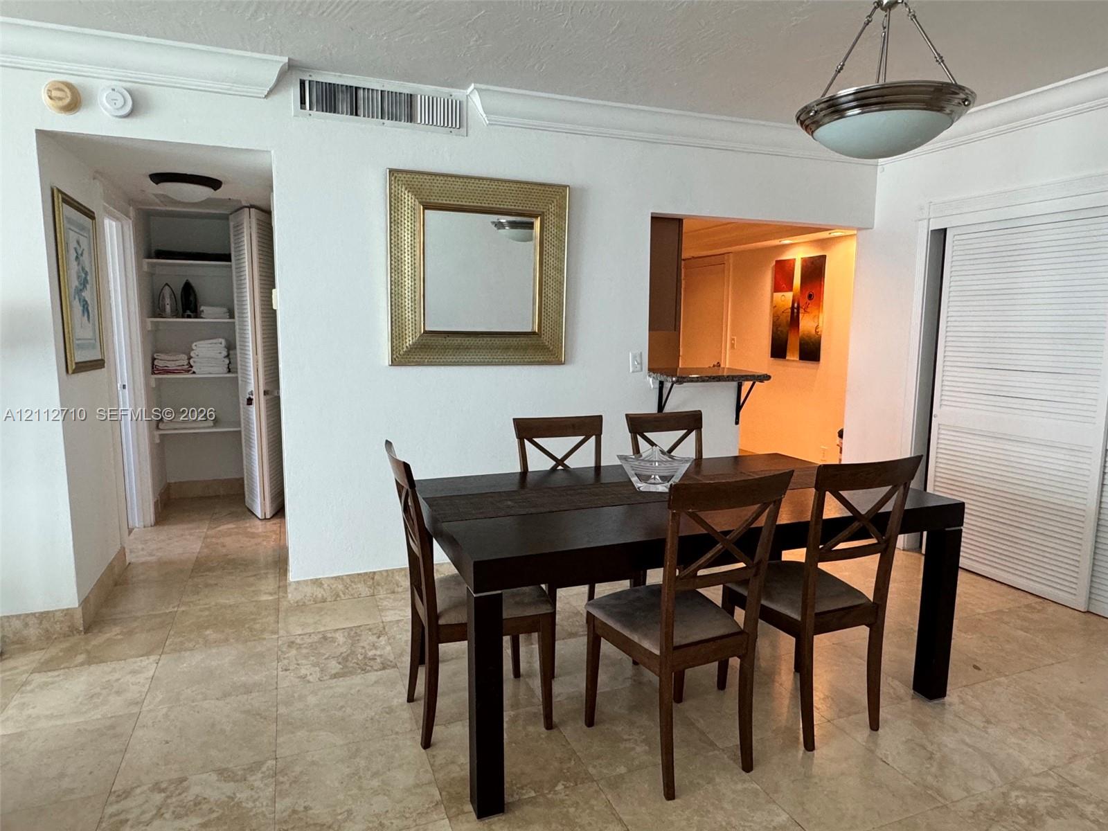 Neutral stone tile flooring, built-in recessed shelving with louvered doors, crown molding, and brushed nickel pendant lighting