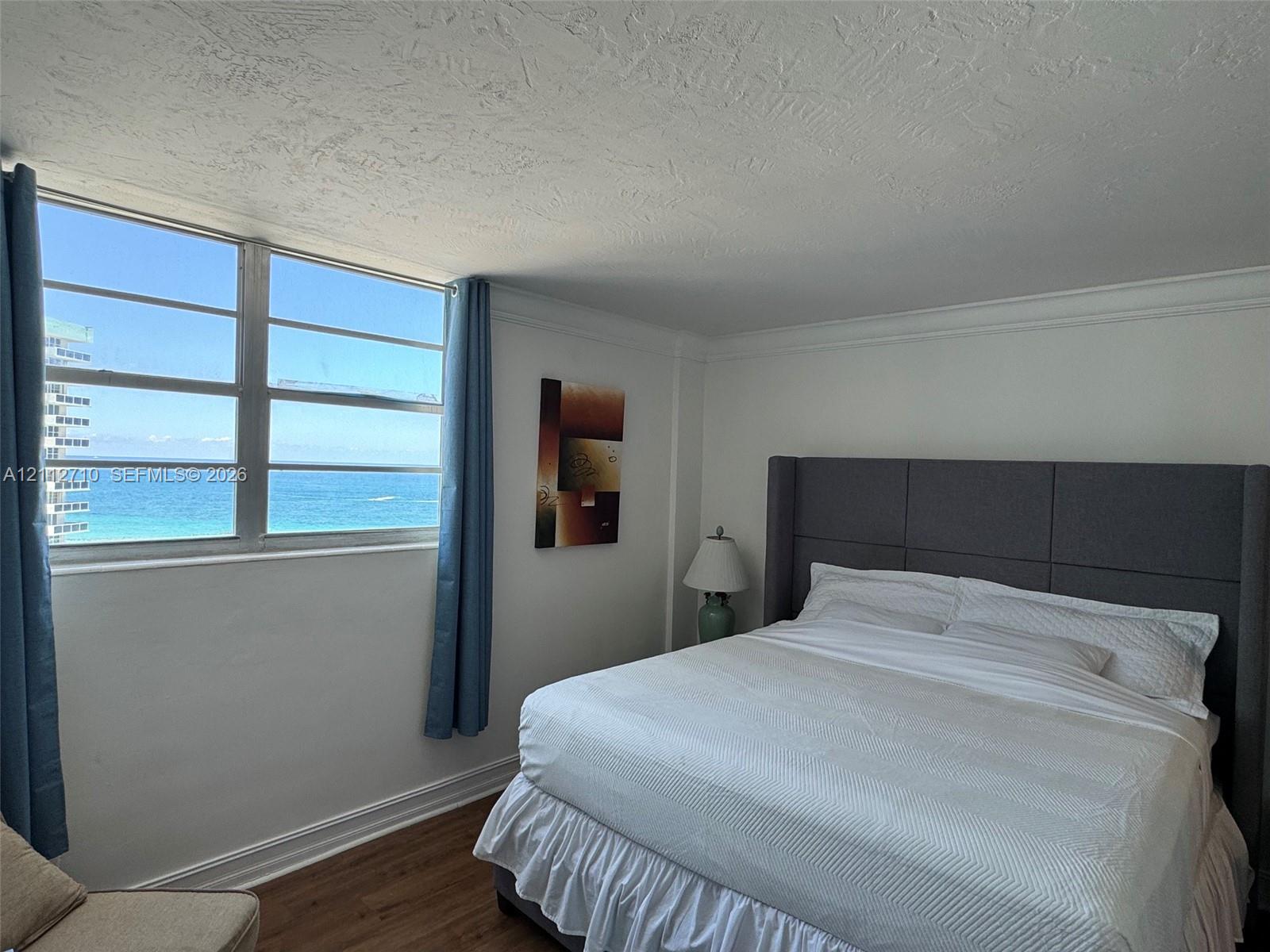 Large multi-pane window with ocean horizon exposure, wood-finish flooring, and crown molding