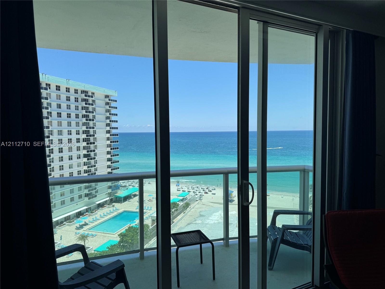 Floor-to-ceiling glass sliding doors opening to a private balcony with glass panel railings, featuring expansive ocean scenery Floor-to-ceiling glass sliding doors opening to a private balcony with glass panel railings, featuring expansive ocean scenery