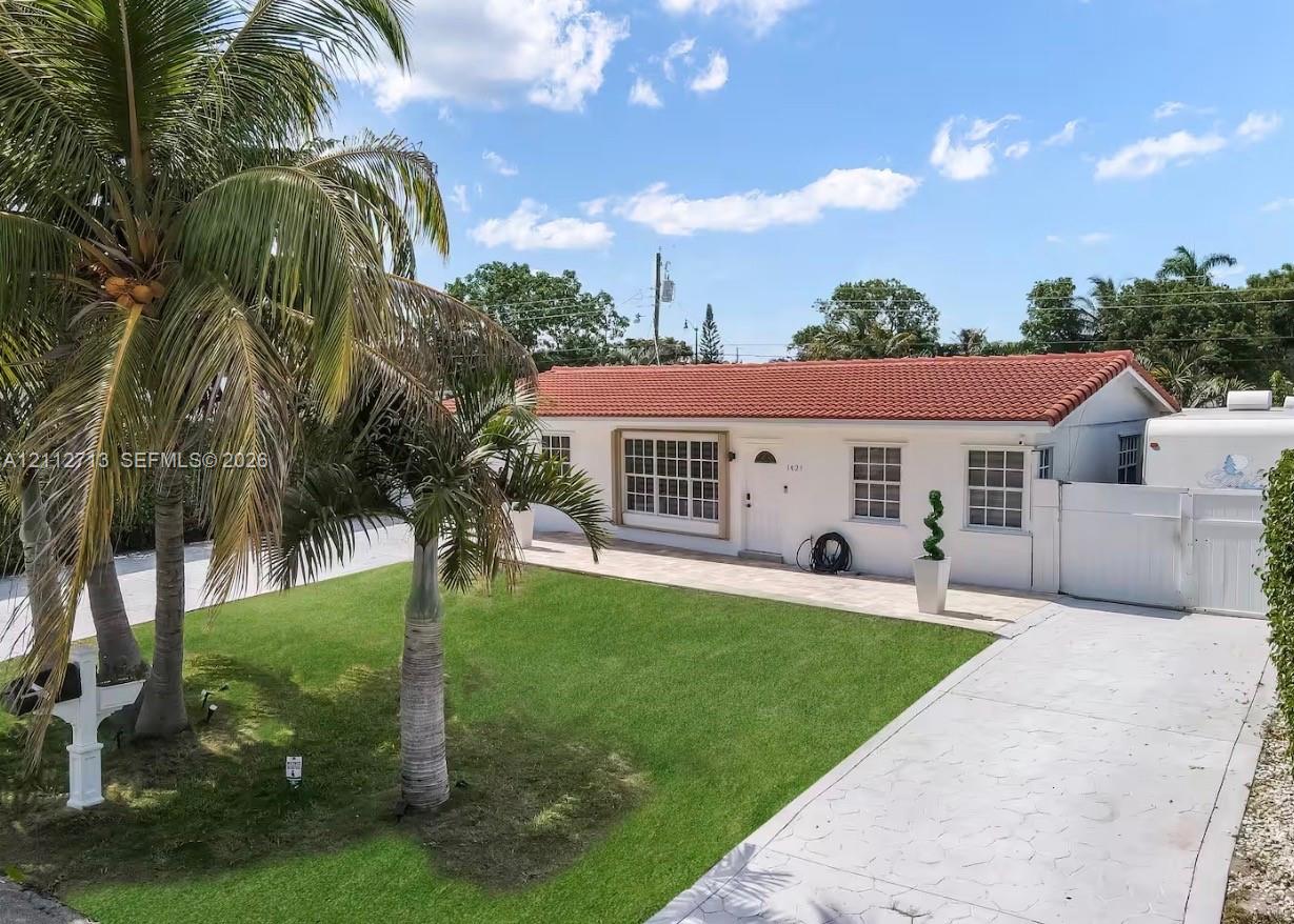Single-story exterior featuring a clay tile roof, white stucco siding, multi-lite windows, and a paved driveway leading to a white perimeter fence