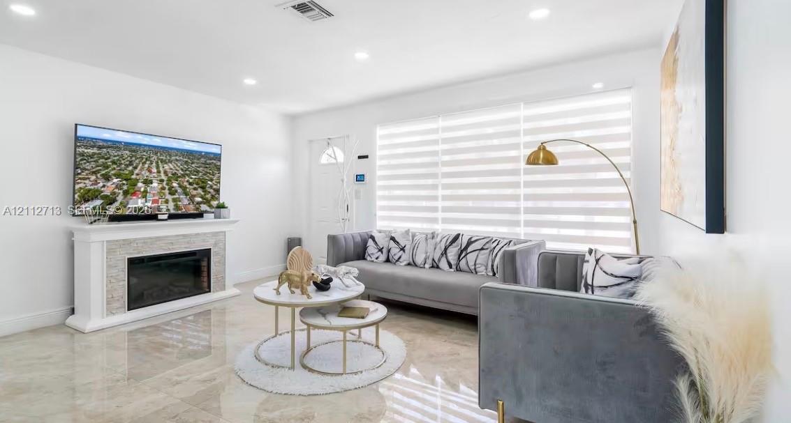 Bright interior featuring large-format tile flooring, recessed lighting, and a fireplace with a stone-textured surround