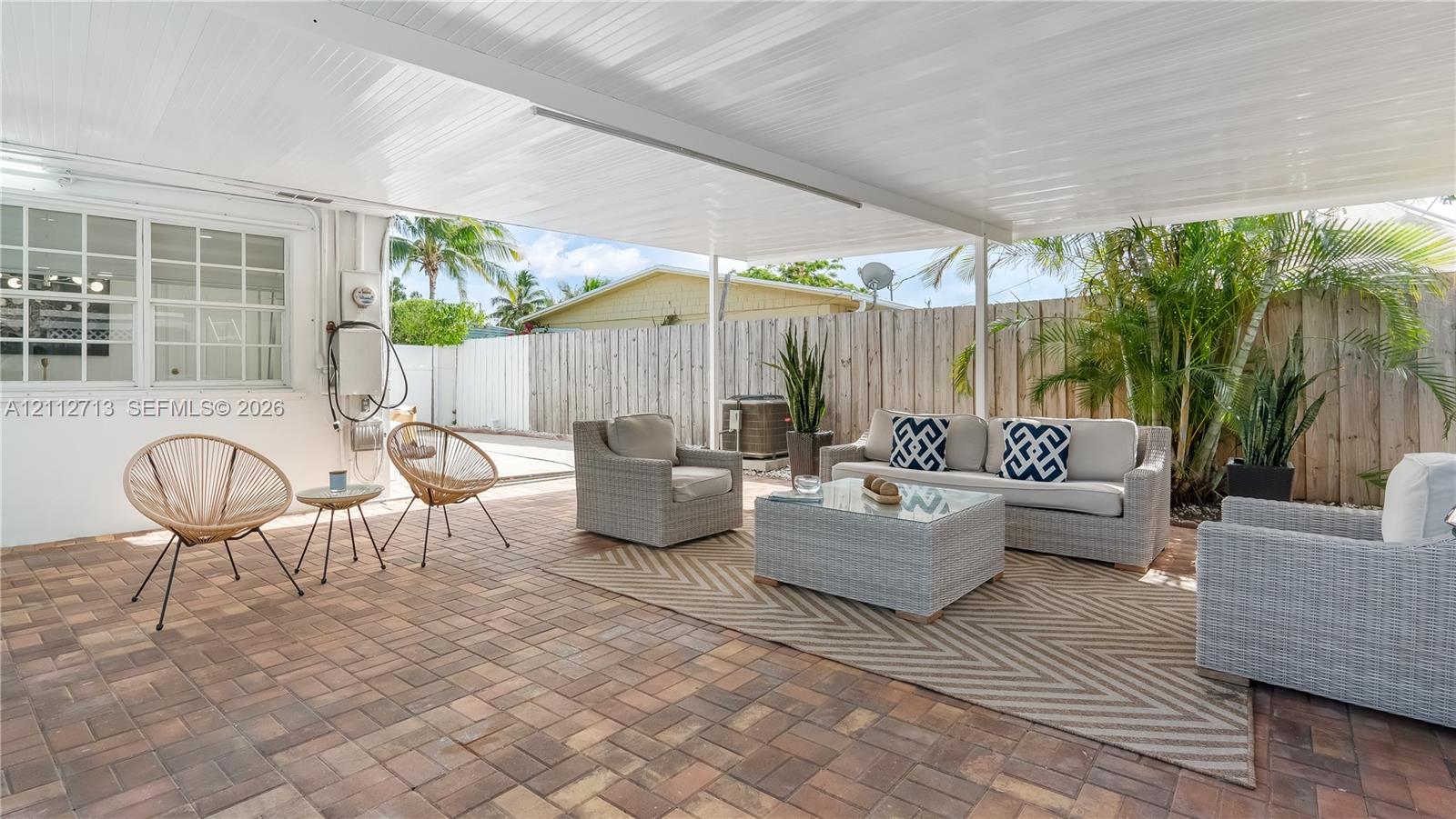 Covered patio featuring multi-tone paver flooring, a white corrugated ceiling, and wood-panel privacy fencing