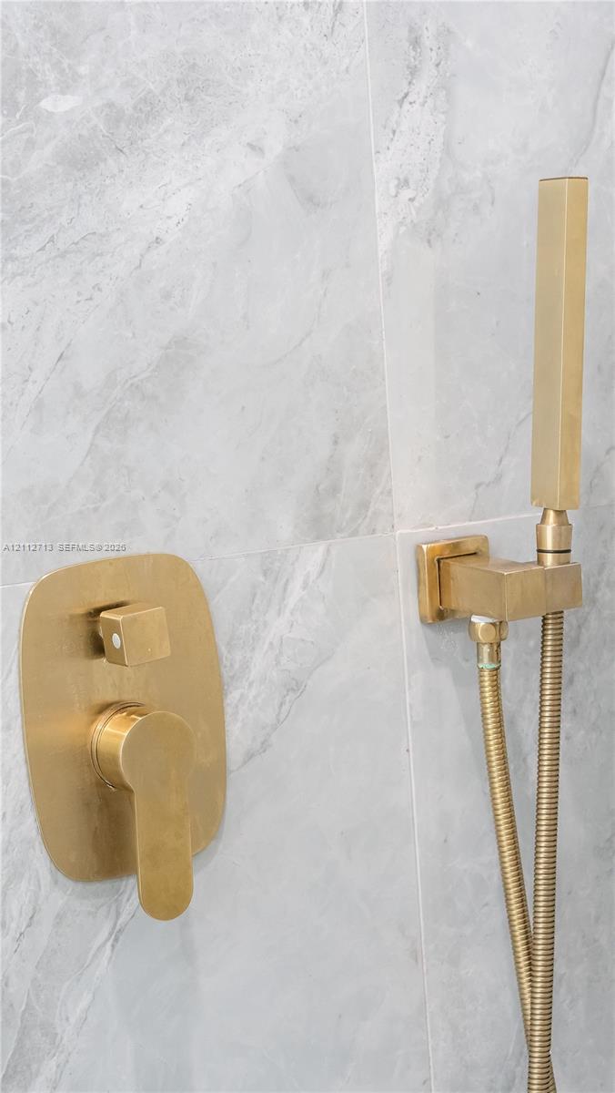 Wall-mounted shower fixture featuring a brushed metallic finish, single-handle mixing valve, and adjustable handheld spray wand, set against large-format, light-toned stone-patterned wall tile