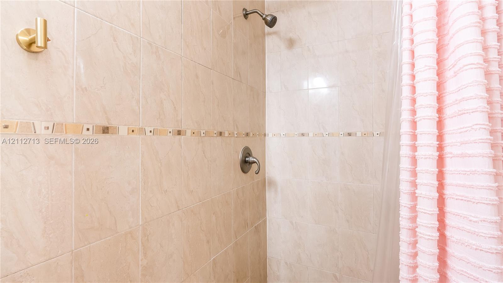 Shower enclosure featuring large-format beige wall tiling, a decorative glass and stone mosaic accent border, and a metallic single-handle pressure-balance valve