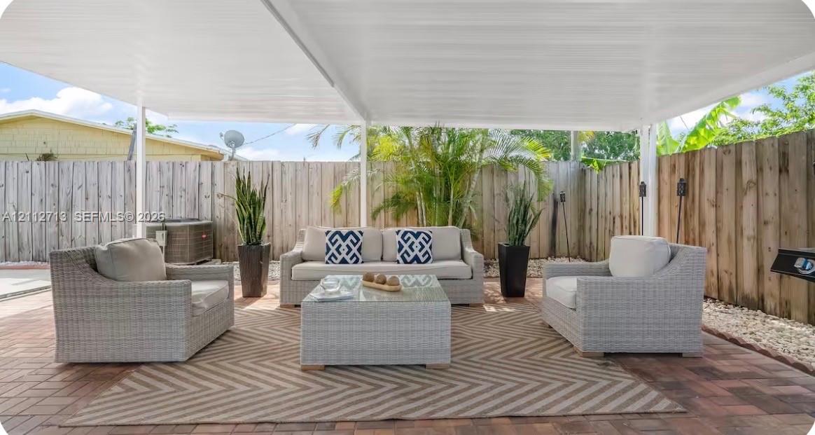 Covered patio featuring a solid-surface overhead structure, concrete paver flooring, and full-height wood-panel privacy fencing