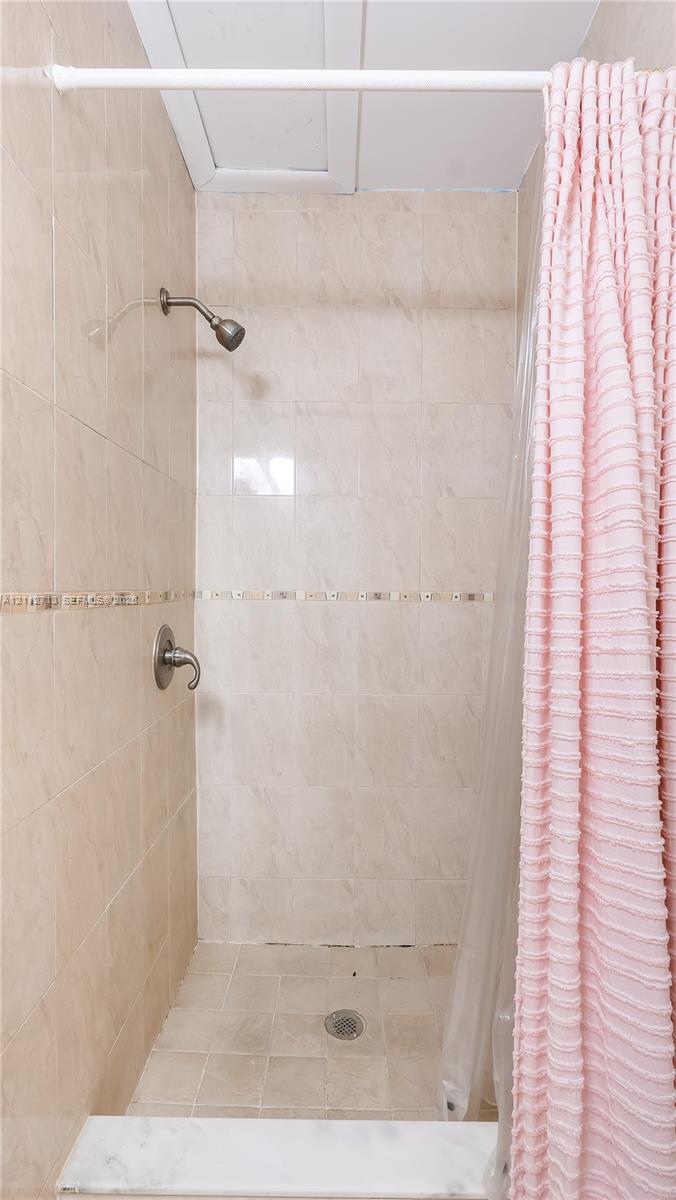 Walk-in shower featuring beige wall and floor tile, a decorative mosaic tile accent border, and a metallic shower fixture