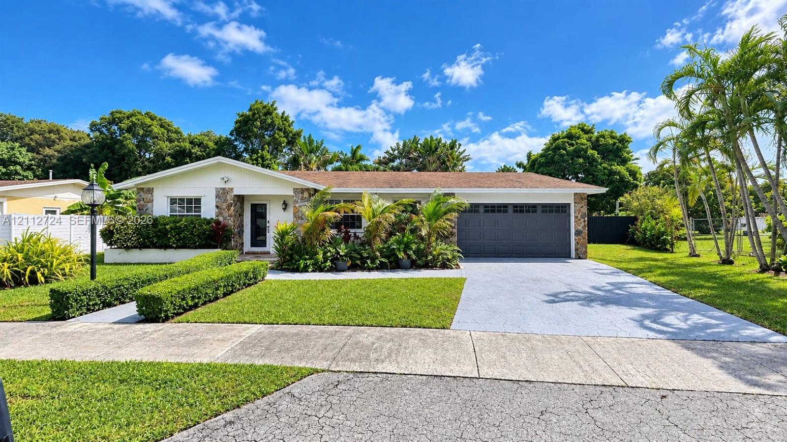 Single-story residence featuring natural stone exterior accents, a grey paneled garage door, a concrete driveway, and manicured landscaping Single-story residence featuring natural stone exterior accents, a grey paneled garage door, a concrete driveway, and manicured landscaping