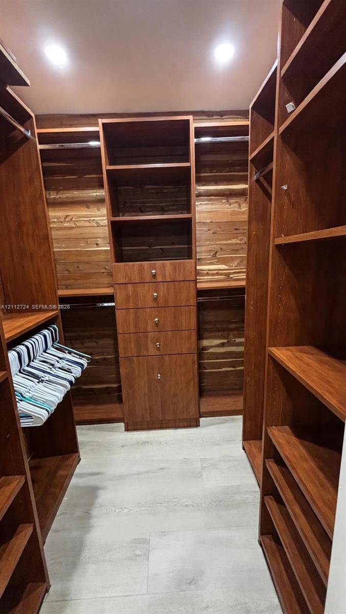 Walk-in closet featuring floor-to-ceiling wood-finish custom cabinetry, a central drawer stack, integrated hanging rods, open shelving, and light-tone wood-finish flooring