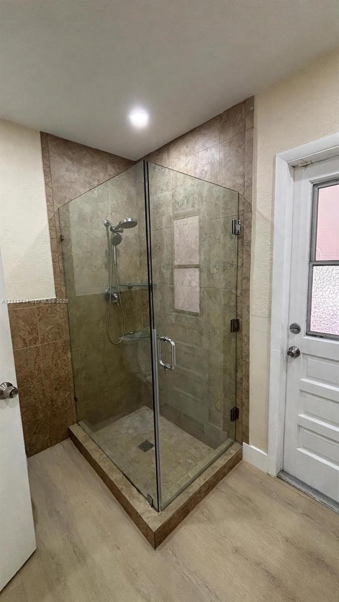 Walk-in shower featuring a frameless glass enclosure, tiled surround, integrated shelving, adjustable handheld shower fixture, and a tiled shower pan