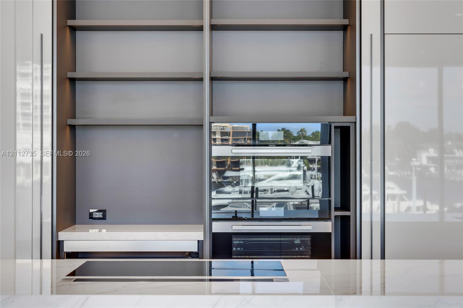 Floor-to-ceiling cabinetry with open shelving, integrated stainless steel double wall ovens, smooth-surface cooktop, and stone countertop