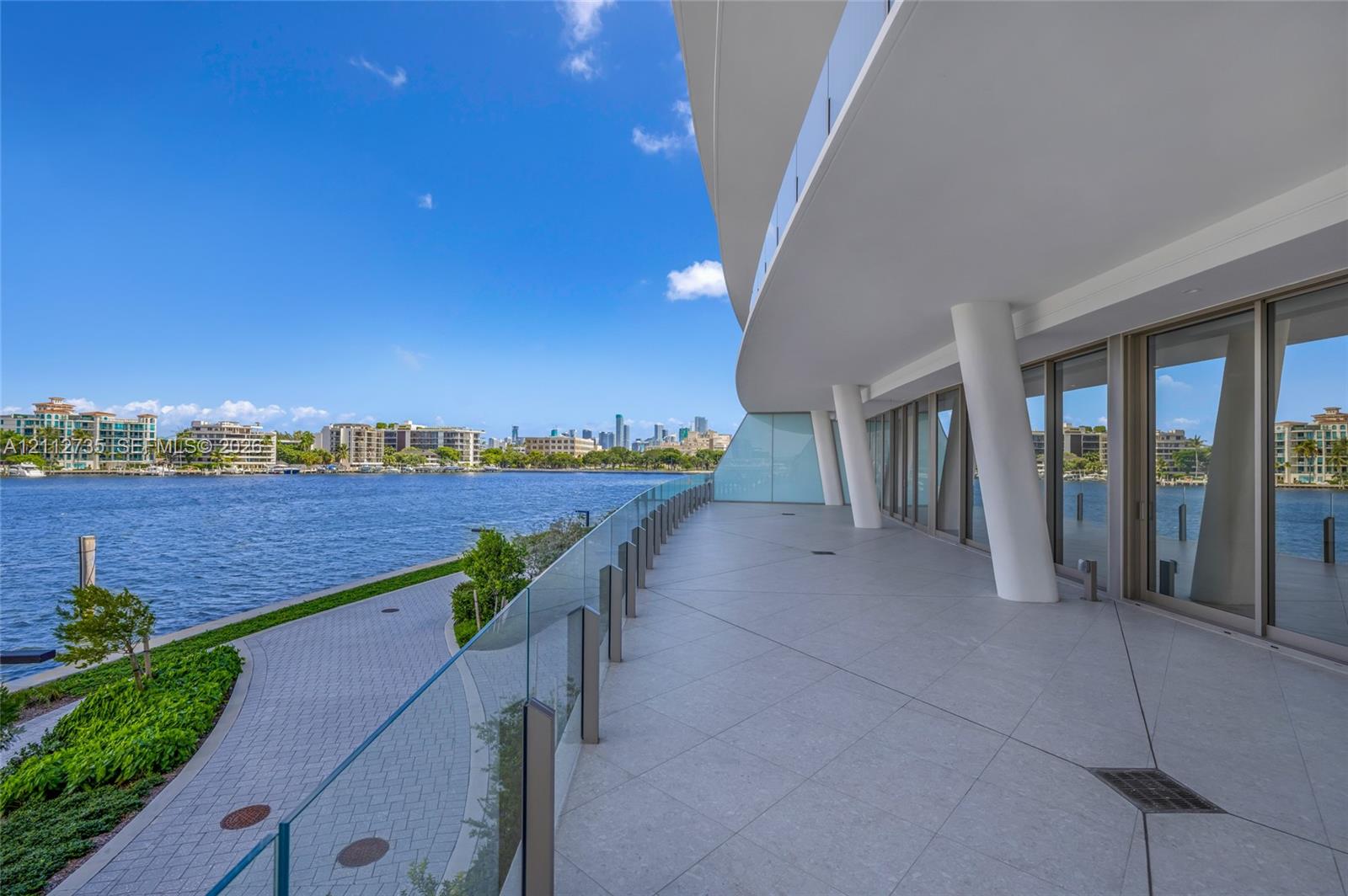 Expansive covered balcony featuring large-format tile flooring, structural support columns, full-height glass sliding doors, and a frameless glass railing
