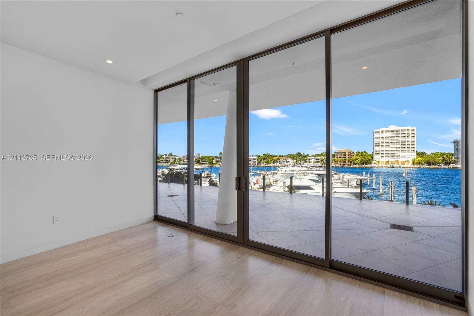 Floor-to-ceiling multi-panel sliding glass doors, wood-finish flooring, recessed lighting, and large format tiled balcony