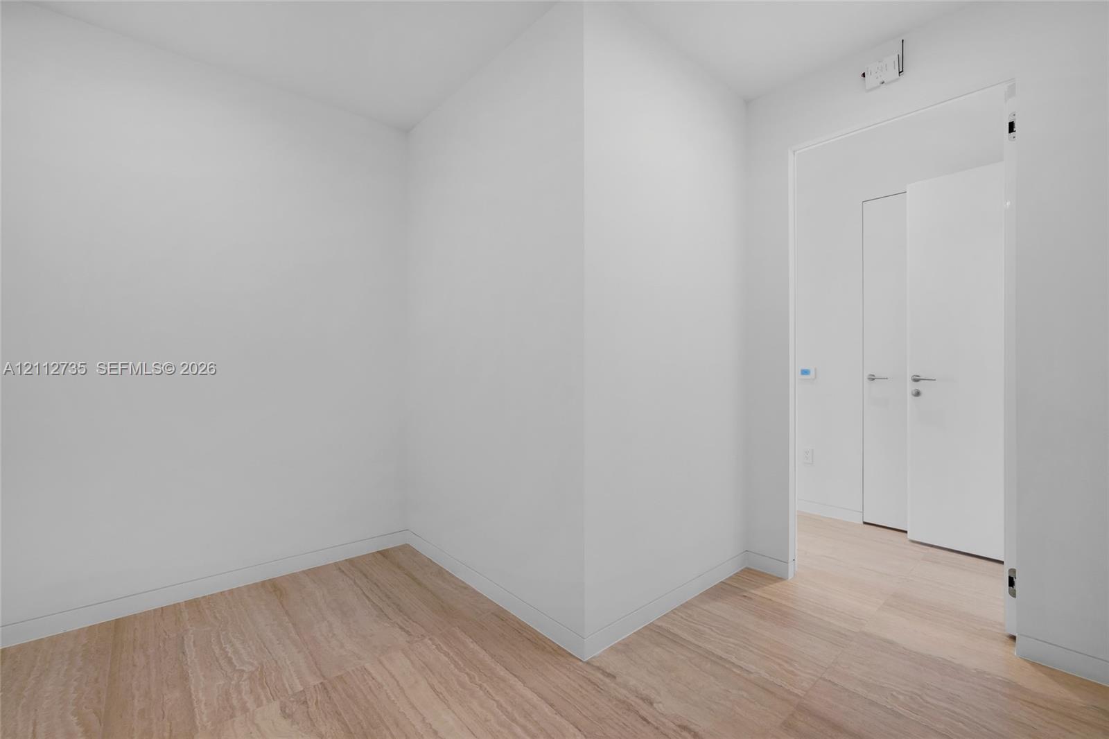 Neutral interior space featuring wood-finish flooring, smooth white wall finishes, and minimalist interior doors with metallic lever handles