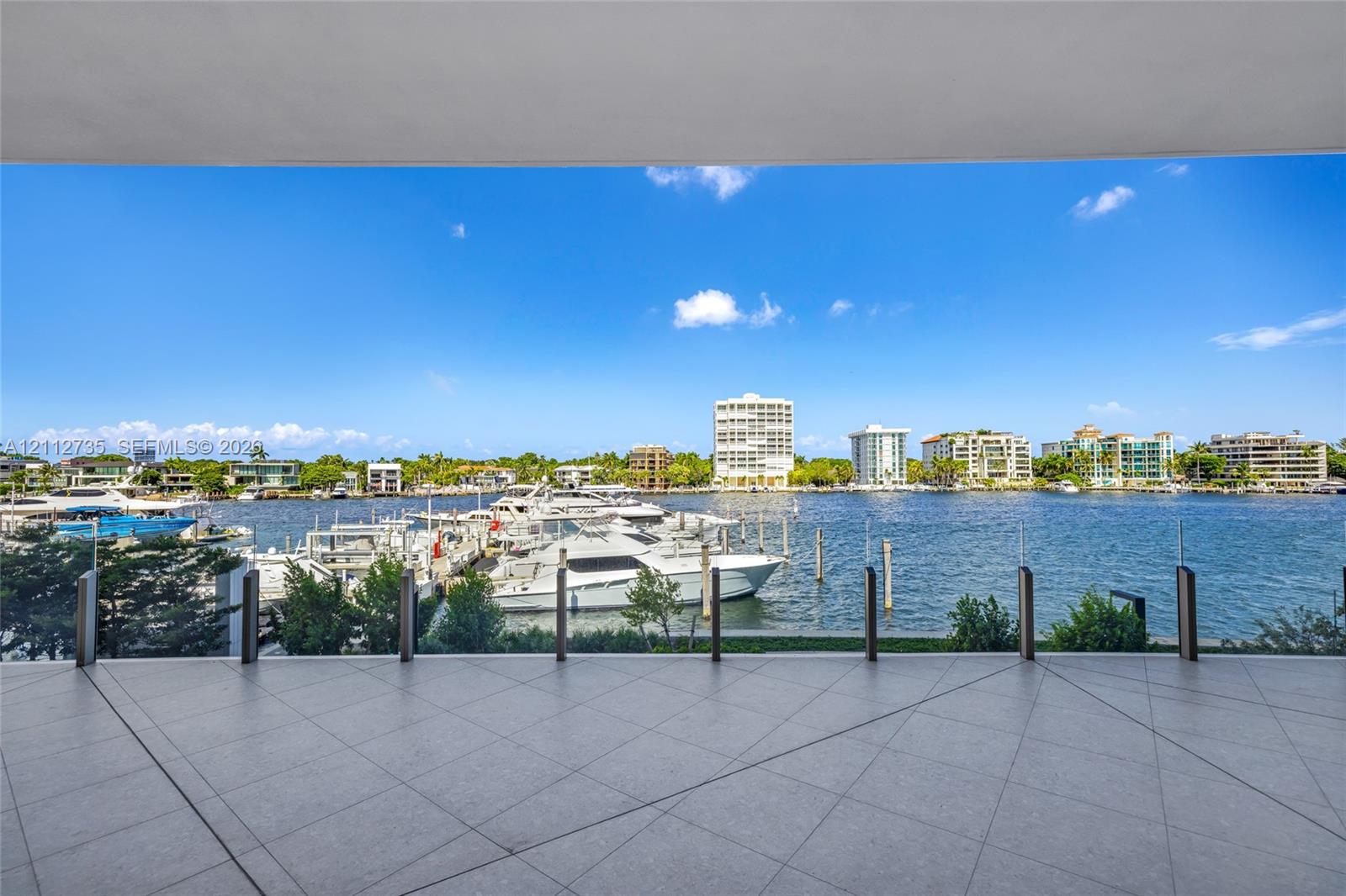 Covered terrace featuring large-format porcelain tile flooring and a transparent glass railing overlooking the waterfront Covered terrace featuring large-format porcelain tile flooring and a transparent glass railing overlooking the waterfront