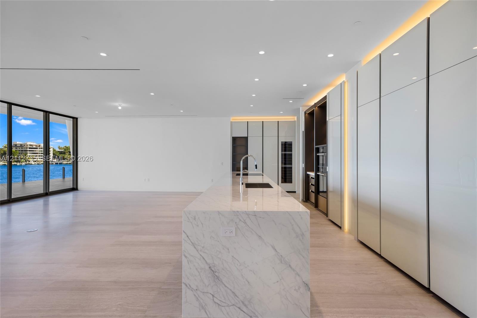 Kitchen featuring a stone-surface island, floor-to-ceiling high-gloss cabinetry, integrated lighting, wood-finish flooring, and expansive glass sliding doors Kitchen featuring a stone-surface island, floor-to-ceiling high-gloss cabinetry, integrated lighting, wood-finish flooring, and expansive glass sliding doors