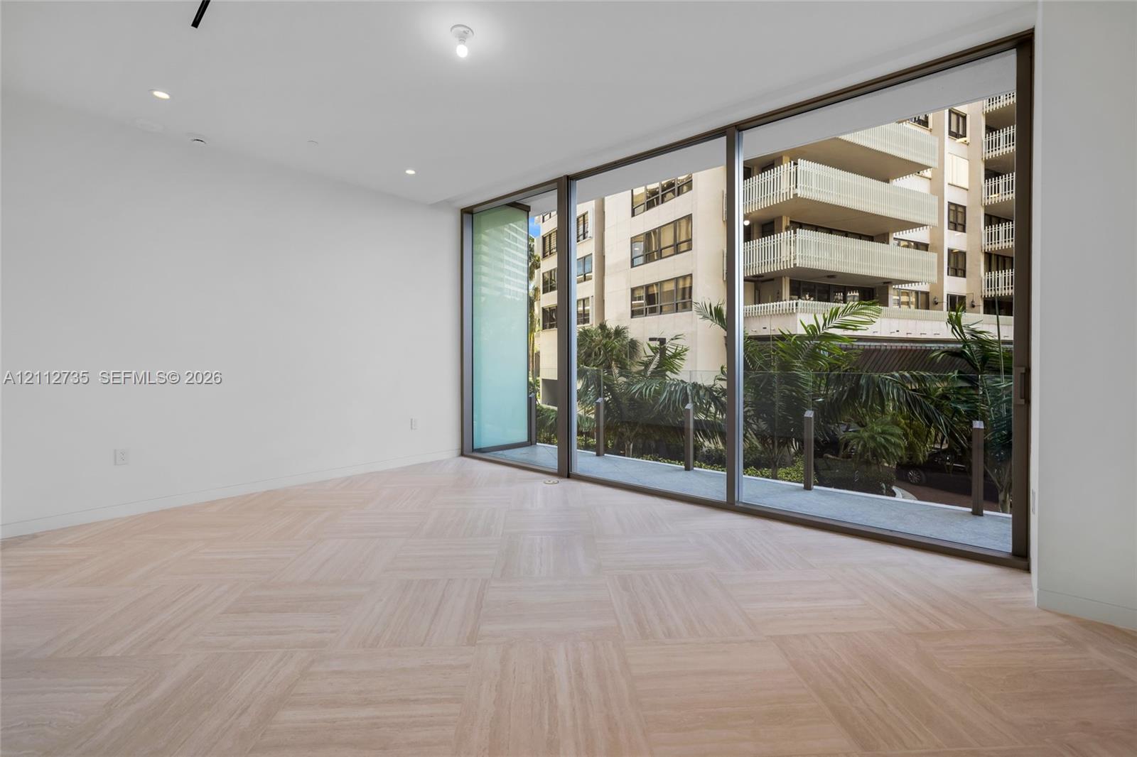Floor-to-ceiling sliding glass panels, herringbone-patterned wood-finish flooring, recessed lighting, and a glass-railed balcony