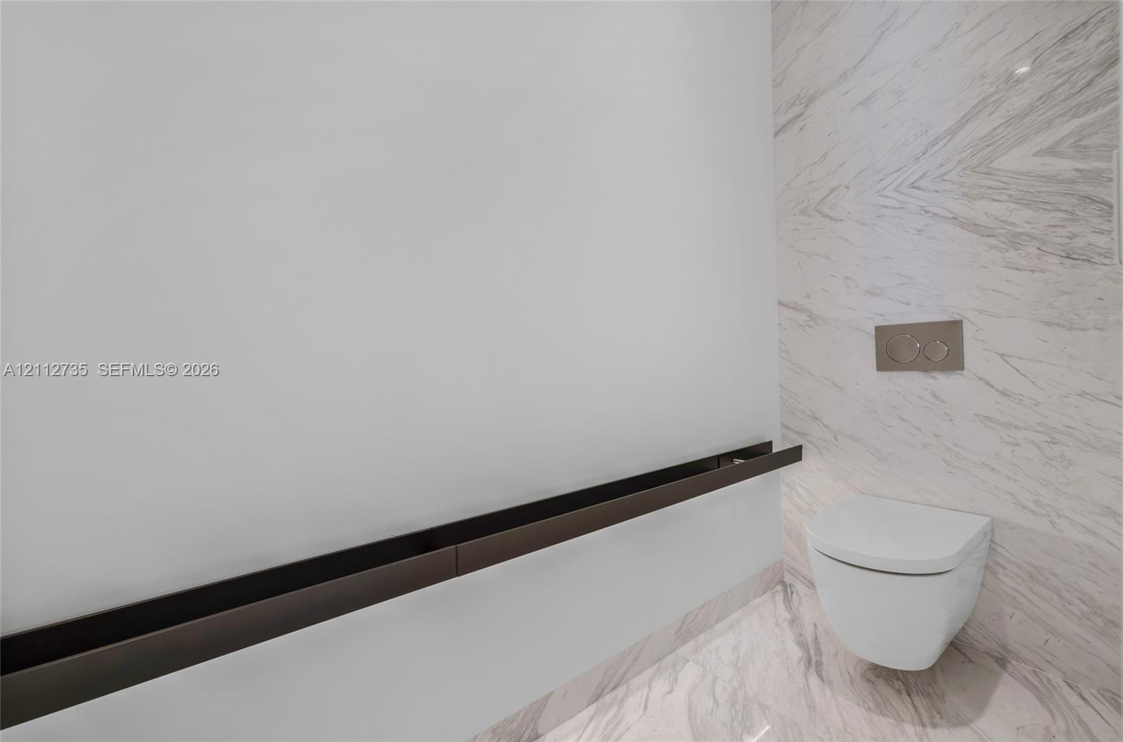 Wall-mounted toilet with a dual-flush actuator, floor-to-ceiling stone-patterned tile wall, and a horizontal dark metal accent trim