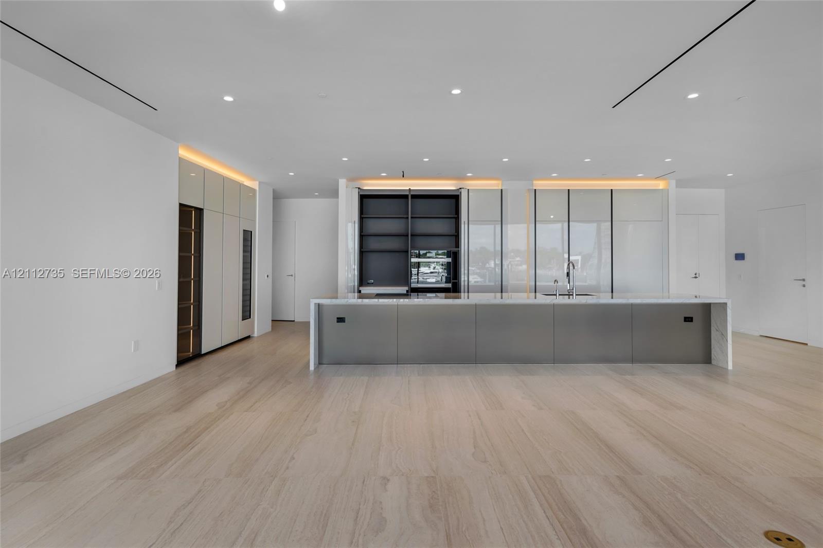 Modern kitchen featuring floor-to-ceiling cabinetry, a sprawling central island with stone-finish countertops, built-in dual wall ovens, recessed linear lighting, and large-format tile flooring