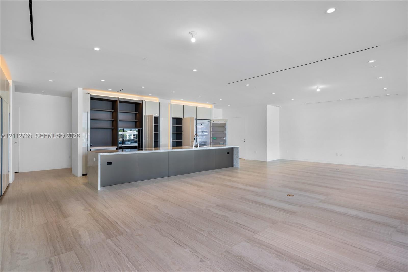 Kitchen featuring an expansive center island with sleek cabinetry, integrated open shelving, recessed ceiling lighting, and continuous wood-finish flooring