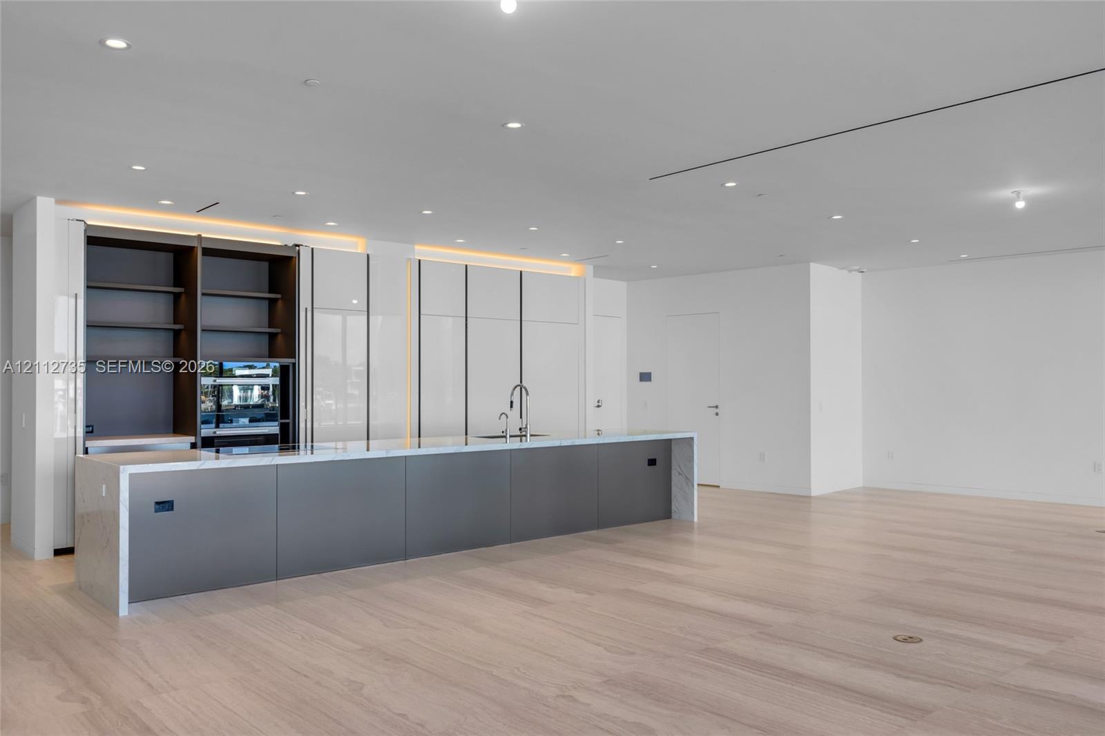 Modern kitchen featuring a expansive island with stone waterfall countertops, high-gloss white cabinetry, integrated open shelving, matte-finish lower cabinetry, and wood-finish flooring