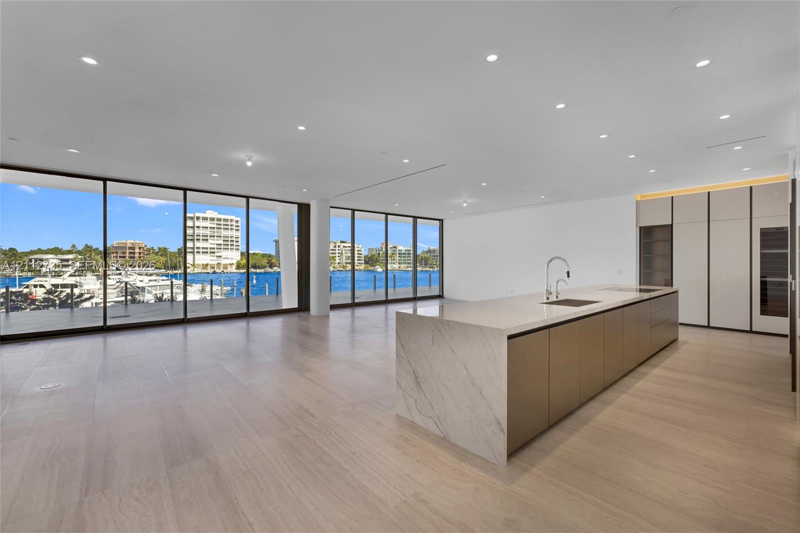 Open-concept interior featuring floor-to-ceiling glass walls, expansive kitchen island with a stone-finish waterfall countertop, built-in floor-to-ceiling cabinetry, and light-toned wood-finish flooring