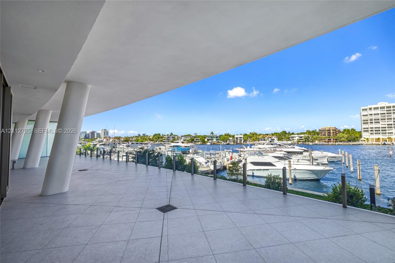 Covered terrace featuring large-format tile flooring, angled structural columns, and a direct water frontage with marina access