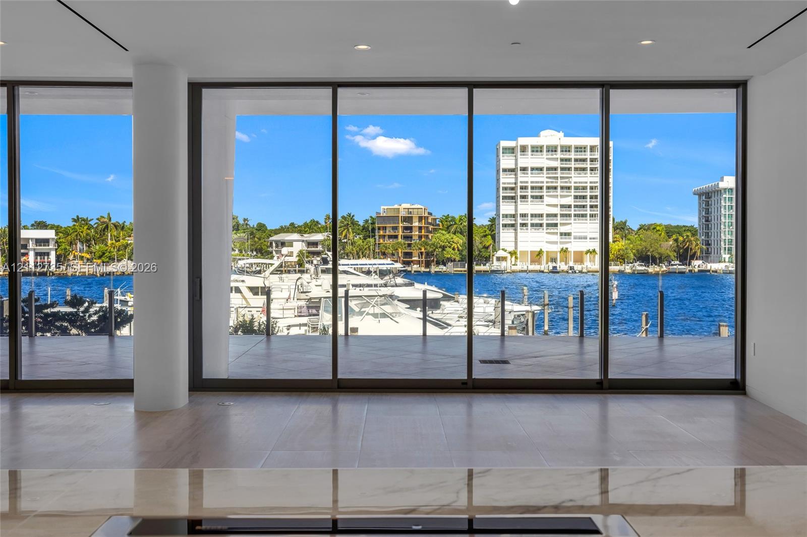 Floor-to-ceiling glass sliding doors, expansive waterfront exposure, polished stone countertop, and light-toned tile flooring