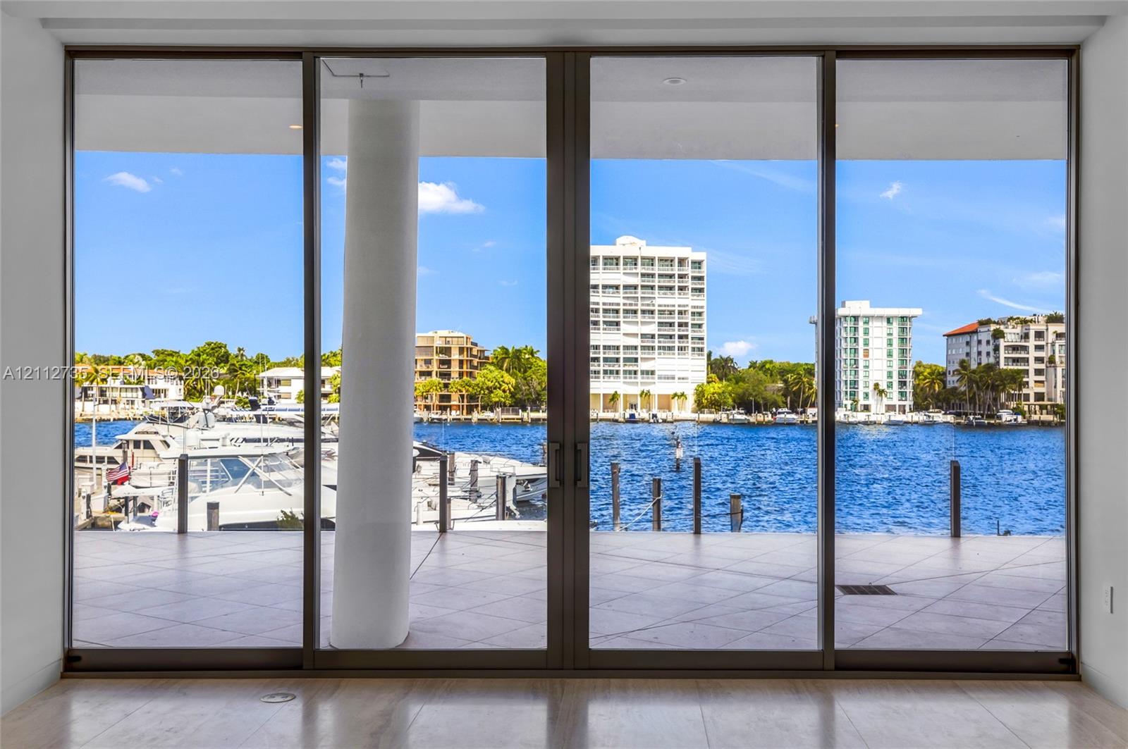 Floor-to-ceiling multi-panel sliding glass doors with dark metal framing, expansive tiled terrace, and structural cylindrical column
