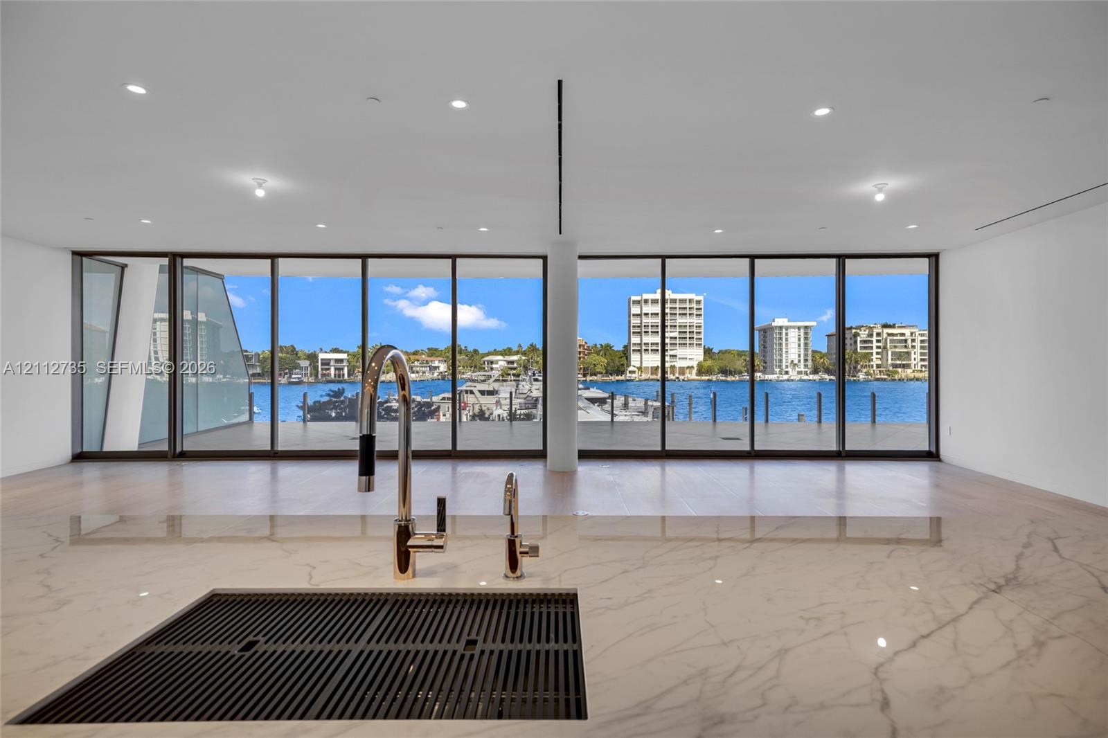 Countertop with an integrated drainboard and high-arc faucet, wood-finish flooring, and expansive floor-to-ceiling glass panels overlooking the waterfront