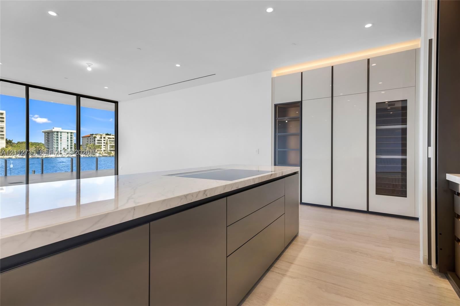 Kitchen featuring a large central island with a stone countertop and integrated cooktop, full-height gloss cabinetry with built-in refrigeration, wood-finish flooring, recessed lighting, and floor-to-ceiling glass doors