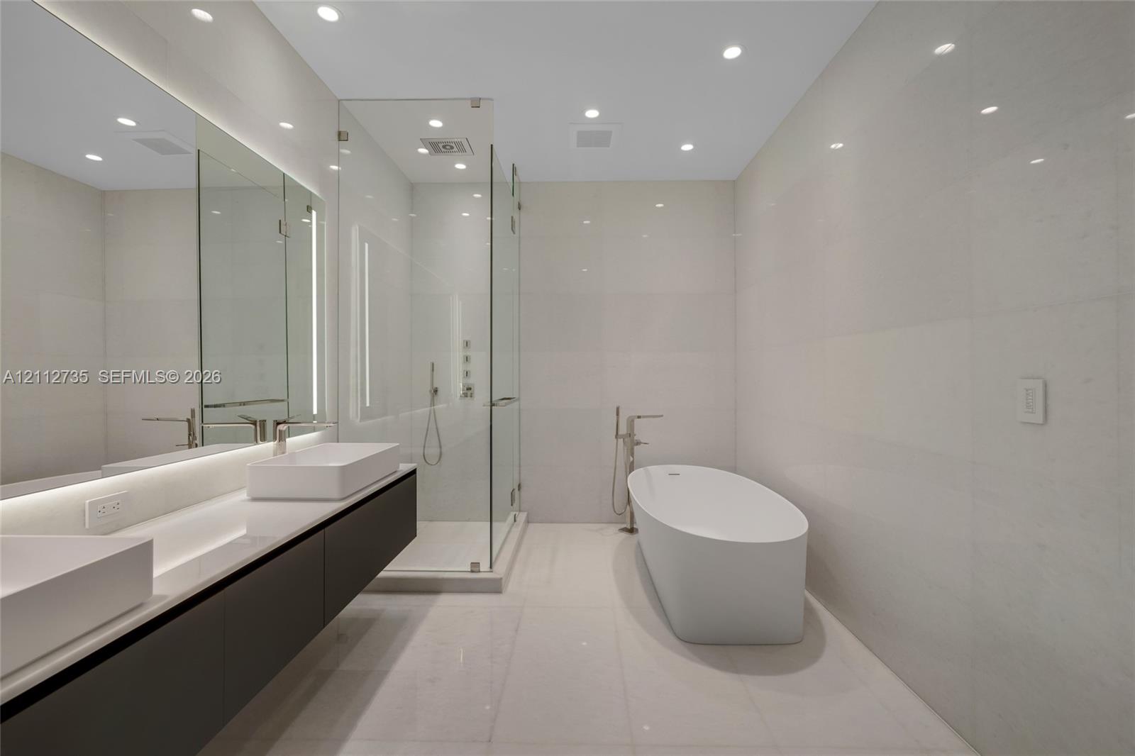 Floating dual vanity featuring rectangular vessel sinks, floor-to-ceiling stone-tiled walls, glass-enclosed shower, and a freestanding soaking tub