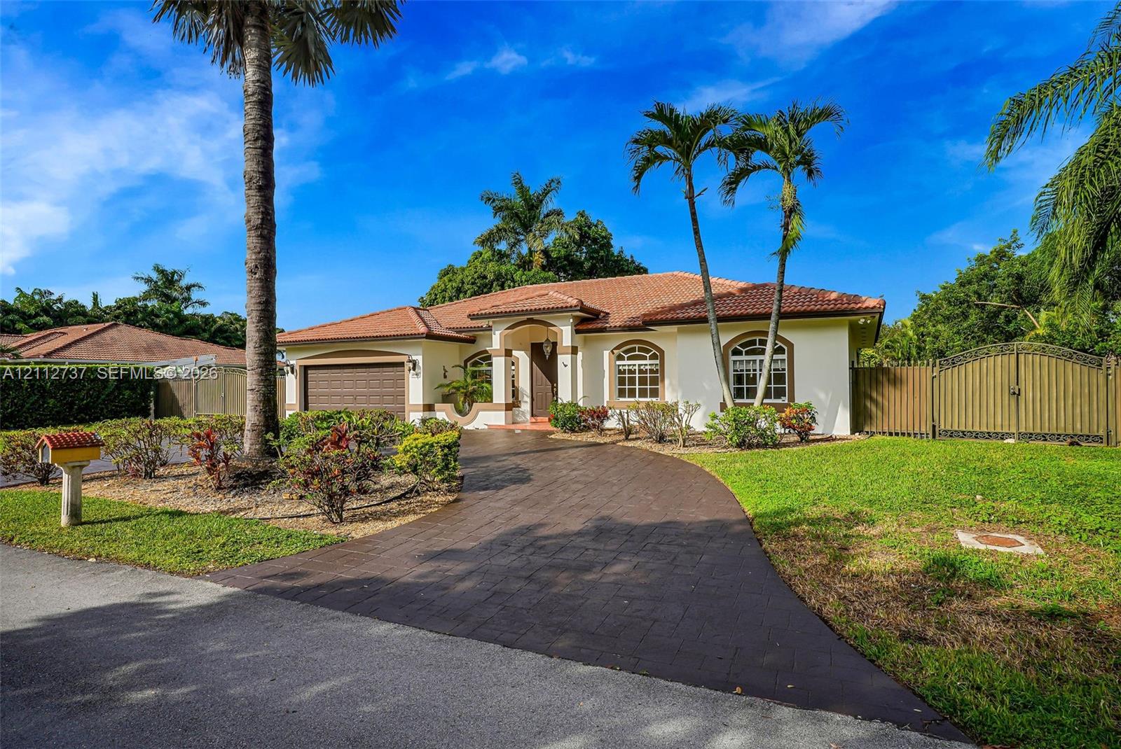Single-story exterior featuring a clay tile roof, arched window detailing, paved driveway, and mature landscaping Single-story exterior featuring a clay tile roof, arched window detailing, paved driveway, and mature landscaping