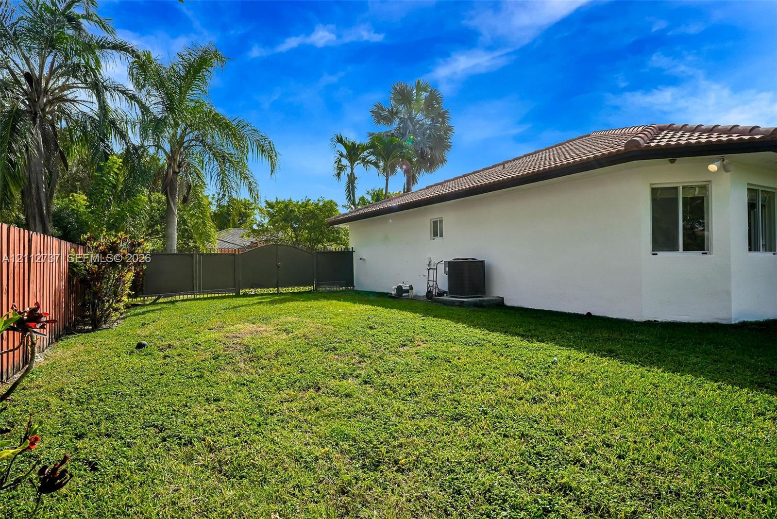 Backyard featuring a manicured lawn, perimeter fencing, and mature palm trees