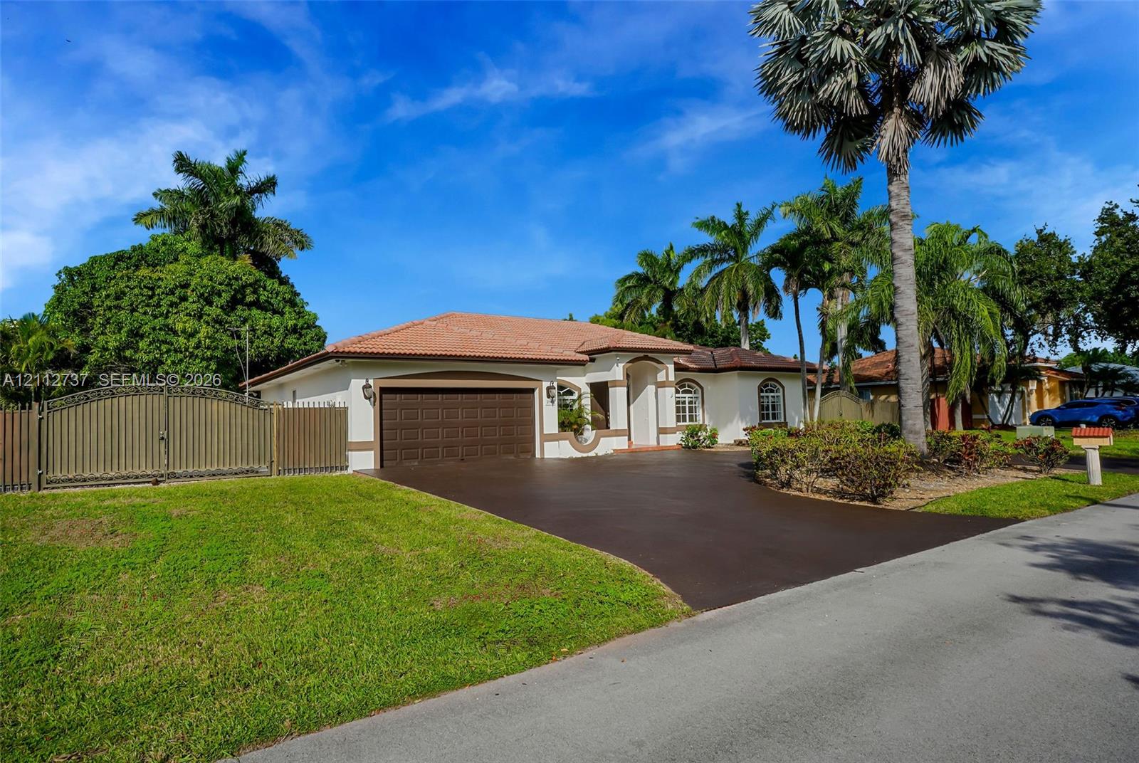 Single-story exterior featuring a clay tile roof, arched entryway, paved driveway, and decorative privacy fencing Single-story exterior featuring a clay tile roof, arched entryway, paved driveway, and decorative privacy fencing