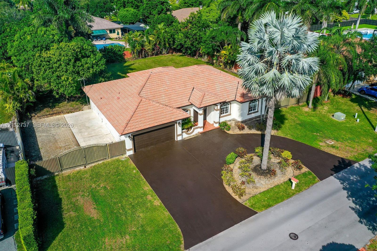 Single-story residence featuring a tiled roof, multi-car garage, expansive paved driveway, and established landscaping Single-story residence featuring a tiled roof, multi-car garage, expansive paved driveway, and established landscaping