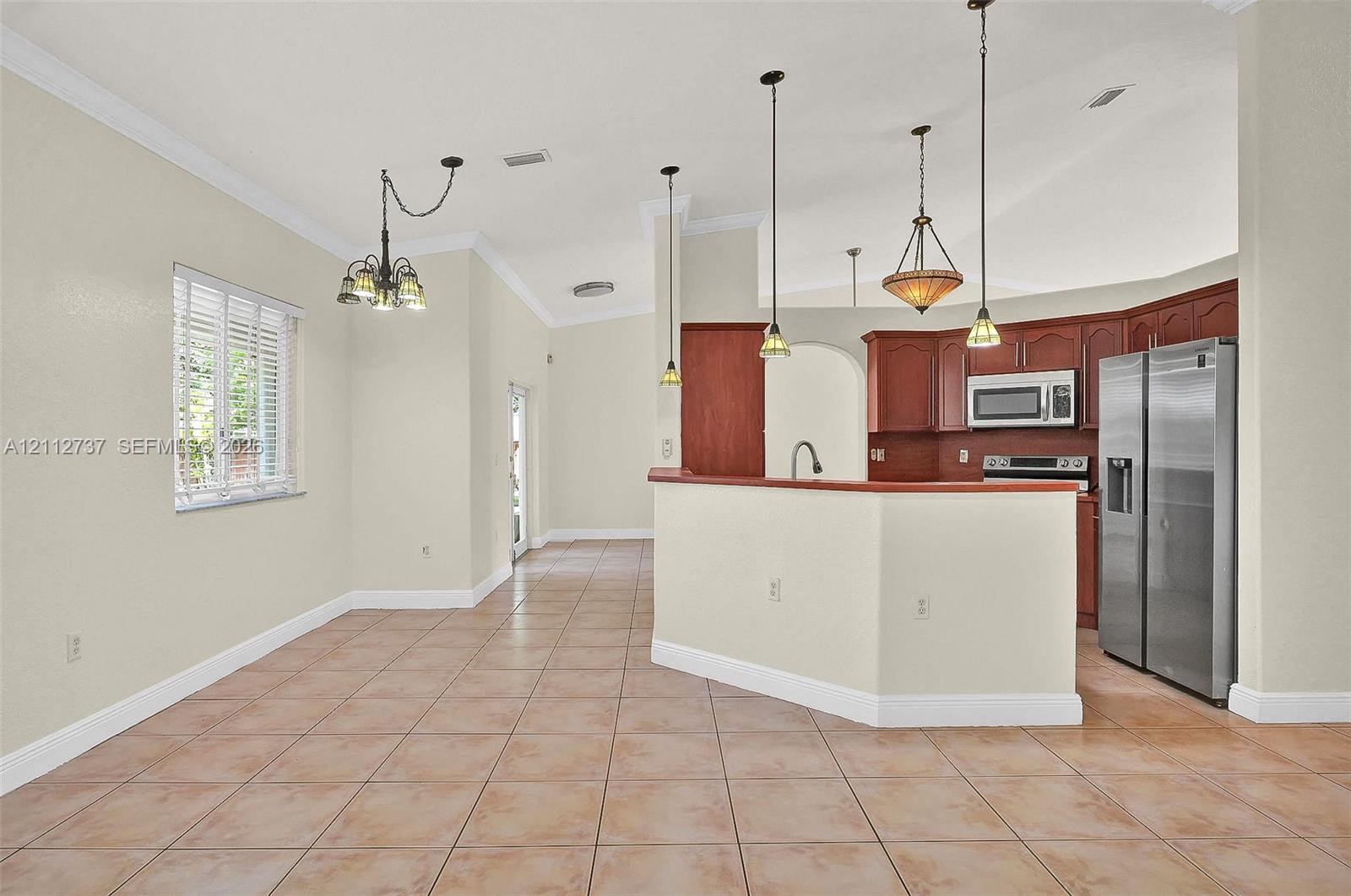 Kitchen featuring wood cabinetry, stainless steel appliances, tile flooring, vaulted ceilings, and multi-pendant lighting
