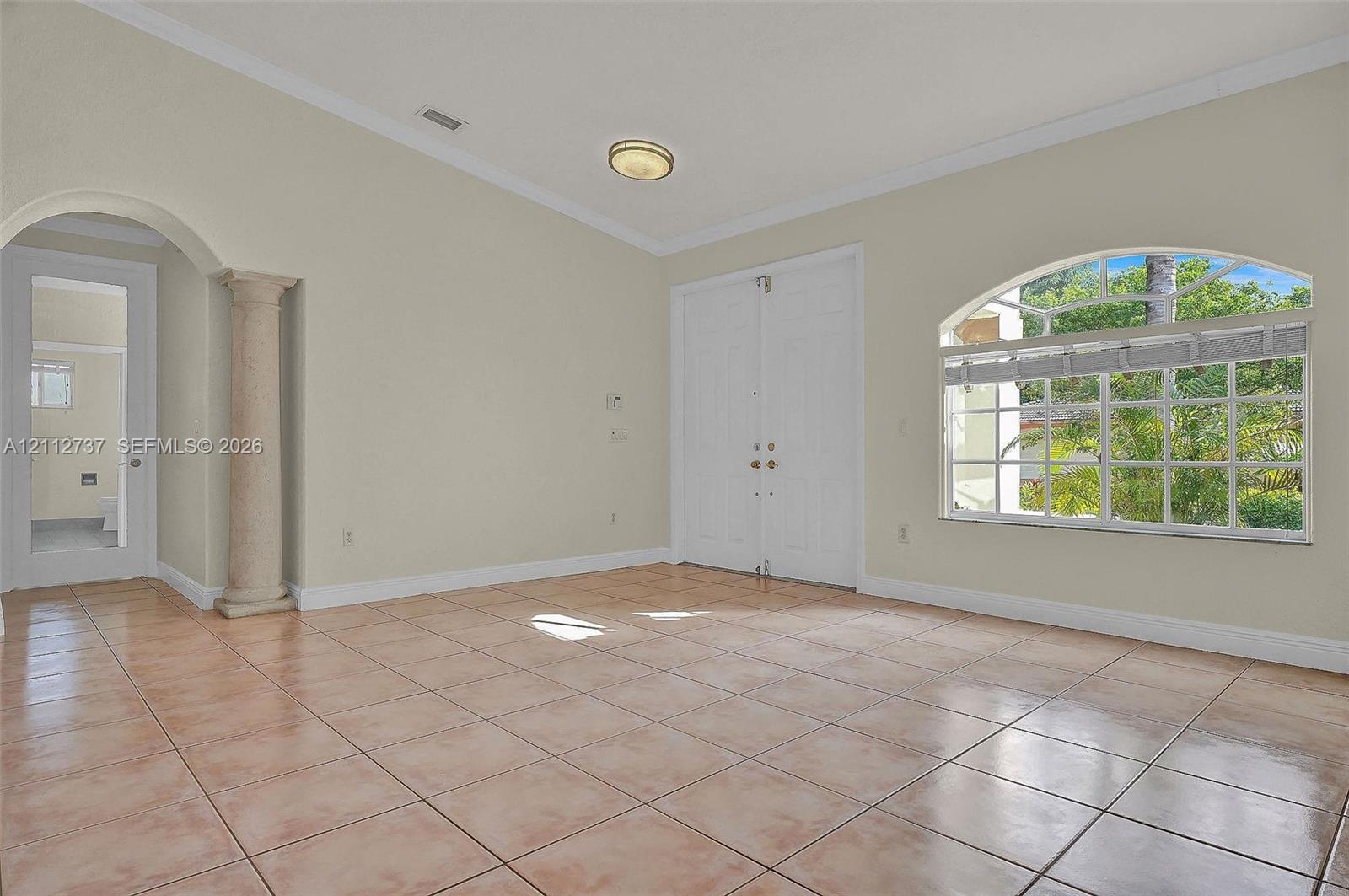 Vaulted ceiling featuring a central architectural column, ceramic tile flooring, arched window with decorative muntins, and double-door entry