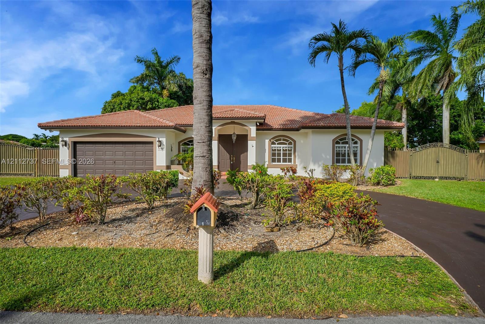 Single-story stucco exterior featuring a tile roof, arched windows, dual-car garage, and mature palm landscaping Single-story stucco exterior featuring a tile roof, arched windows, dual-car garage, and mature palm landscaping