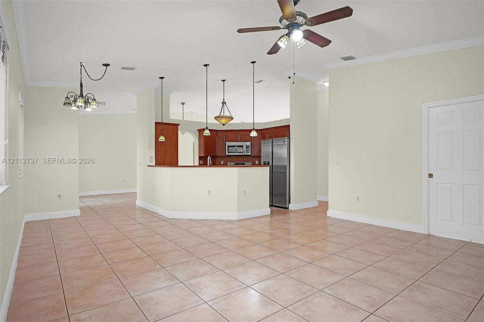 Open-concept interior featuring ceramic tile flooring, tray ceilings, dark-finish cabinetry, built-in stainless steel appliances, and multi-light hanging fixtures