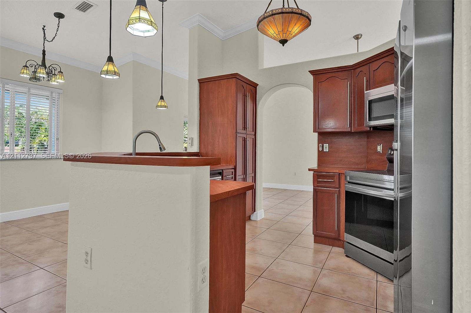 Kitchen featuring wood cabinetry, stainless steel appliances, tile flooring, and multi-light pendant fixtures