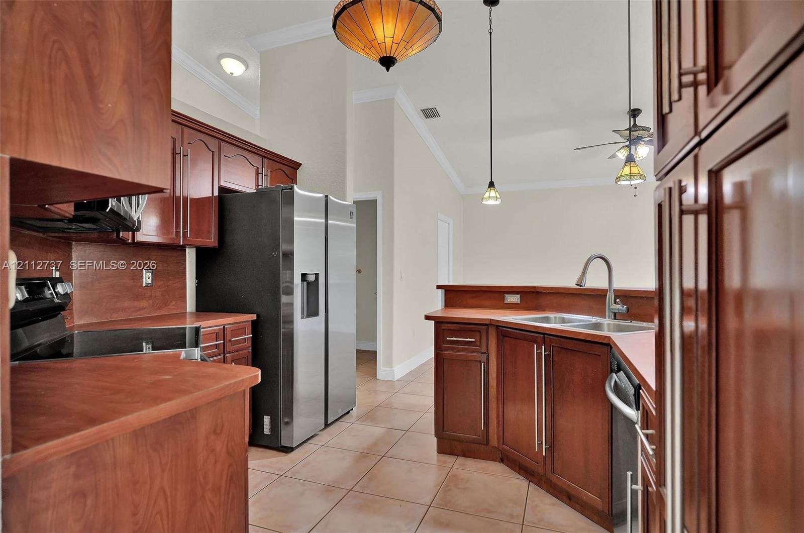 Kitchen featuring cherry-finish cabinetry, stainless steel appliances, ceramic tile flooring, vaulted ceilings, and decorative pendant lighting