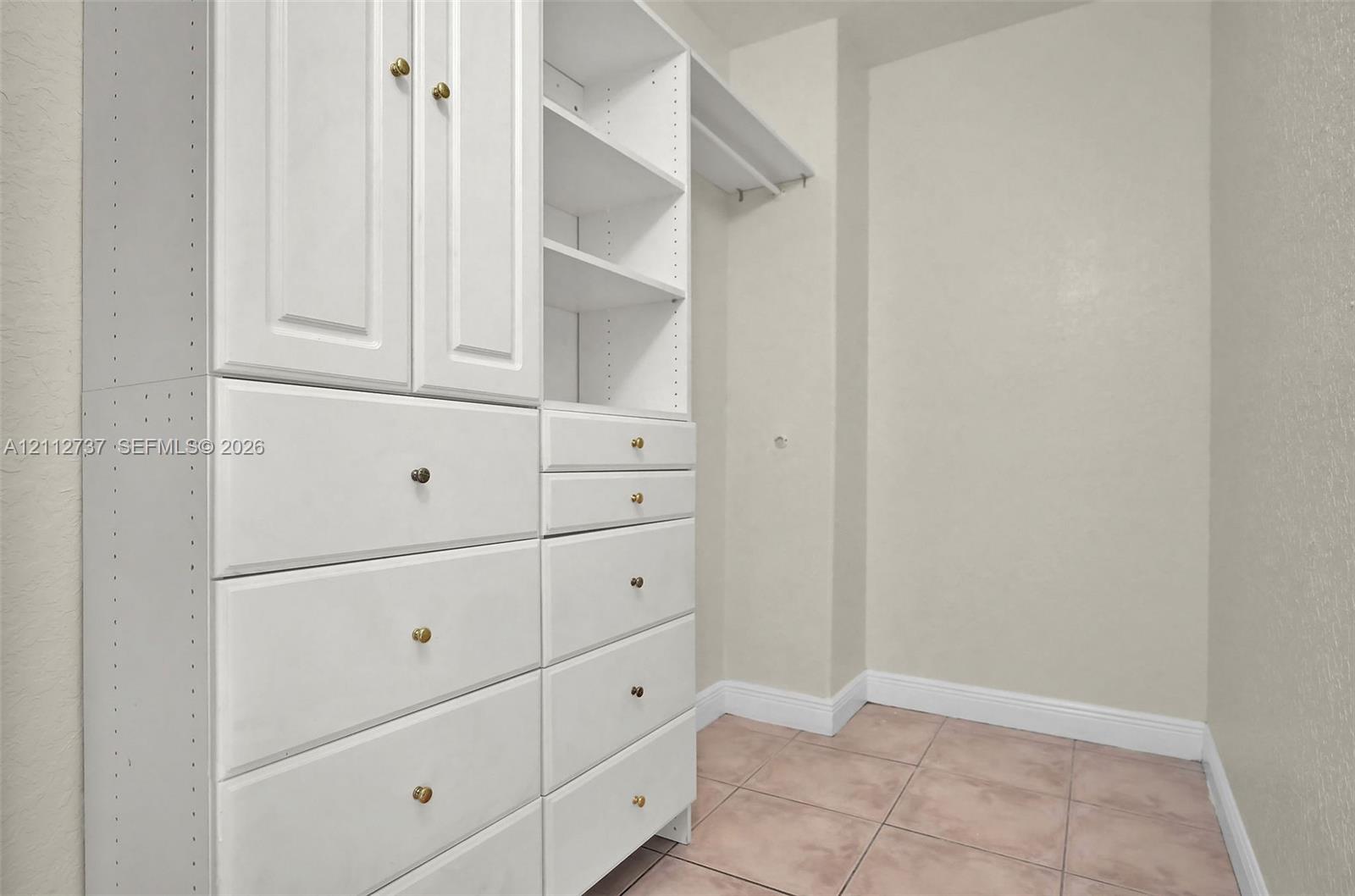 Built-in storage system featuring white cabinetry, tiered shelving, integrated drawers, and tile flooring